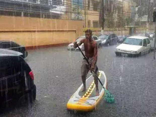 Morador anda de stand up no meio de rua alagada em São Vicente, SP. (Foto: Junior Fernandes/ Arquivo Pessoal.)