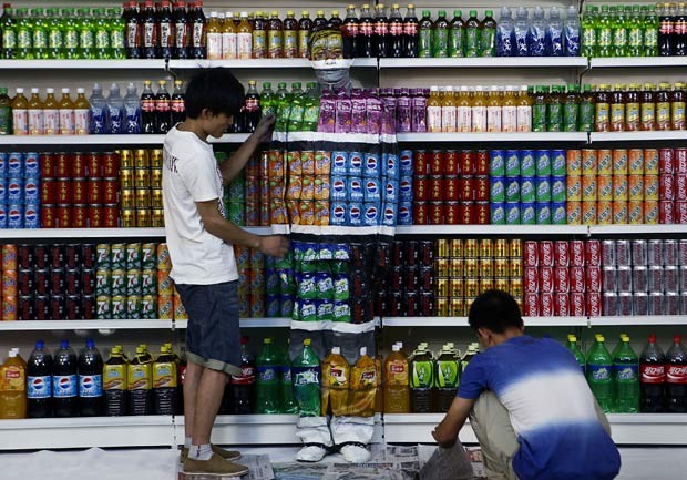 Com a ajuda de dois assistentes, Liu Bolin se pinta em agosto de 2011 para ficar oculto na frente de refrigerantes de um mercado (Foto: AP)