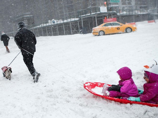 Homem caminha na neve e puxa prancha com duas crianças perto do Central Park, em Nova York (Foto: KENA BETANCUR / AFP)