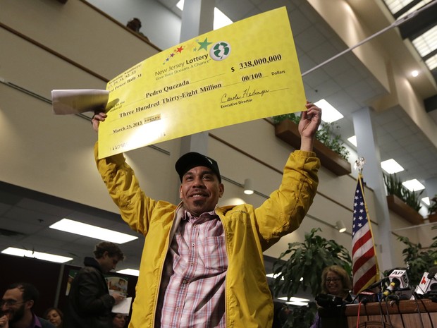 Pedro Quezada, o vencedor do prêmio principal da Powerball, segura o cheque promocional durante uma coletiva de imprensa na lotérica de Nova Jersey (Foto: AP Photo / Julio Cortez))