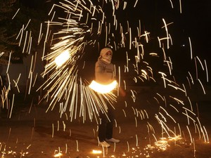 Jovem brinca com fogos de artifício em Nablus, na Cisjordânia, enquanto outras pessoas acompanham o discurso do presidente palestino, Mahmud Abbas, transmitido direto de Nova York (Foto: Nasser Ishtayeh/AP)