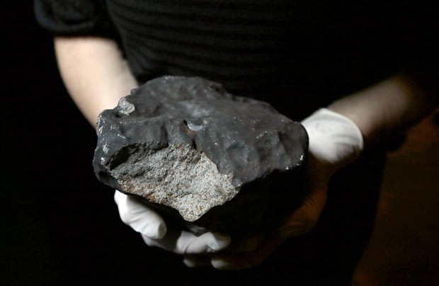 Funcionário do Museu Nacional de História Natural de Paris mostra nesta quinta-feira (14) meteorito de 5,2 quilogramas, um dos que caíram em 2011 em Draveil, no departamento de Essonne, a cerca de 80 quilômetros de Paris (Foto: Jacques Demarthon/AFP)