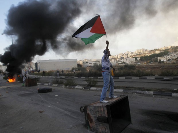 Palestino ergue bandeira durante confrontos com forças de segurança israelenses perto de Ramallah (Foto: Reprodução)