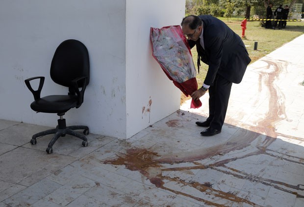 Membro do Parlamento coloca flores em local com rastro de sangue deixado após atentado a museu na Tunísia (Foto: Christophe Ena/AP)