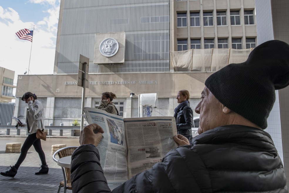 Homem lê jornal em café com embaixada americana em Tel Aviv à sua frente (Foto: Reuters/Baz Ratner)