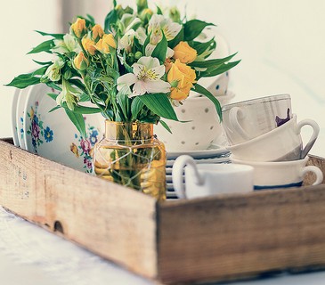 O arranjo de flores ajuda a inovar ao usar o caixote de frutas para  abrigar louças desparceiradas do chá da tarde