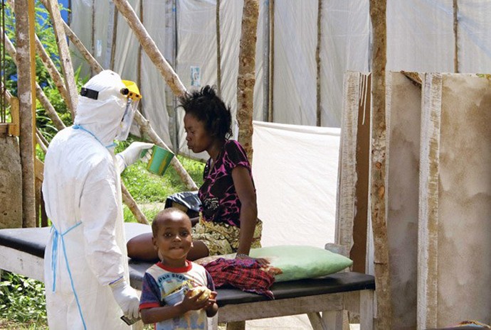 Profissional da saúde, usando proteção especial, dá água a mulher com ebola, em um centro de tratamentos para infectados no Hospital Governamental de Kenema, em Serra Leoa