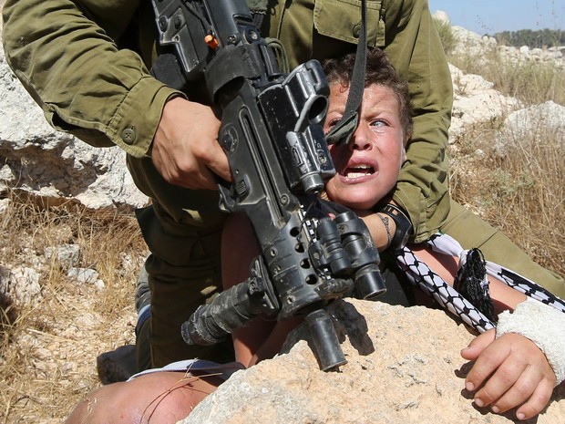 Soldado armado imobiliza um menino palestino durante confronto entre forças de segurança de Israel e manifestantes palestinos ocorrido depois de marcha contra o confisco de terras palestinas para expandir assentamentos judeus em Nabi Saleh, Cisjordânia (Foto: Abbas Momani/AFP)