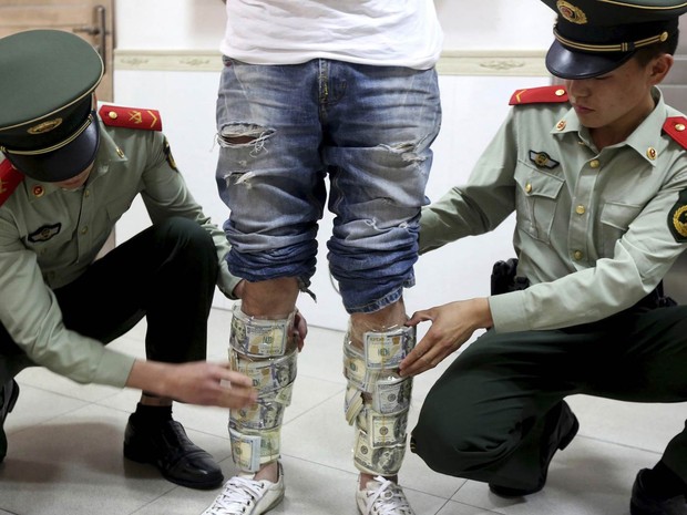 Policiais paramilitares removem Maços Opaco somam EUA $ 580 Milhões Presos como canelas de hum Homem detido na Fronteira de Hong Kong com Shenzhen, na China.  O Homem tentava traficar uma fortuna parágrafo Dentro da Região Administrativa Especial de Hong Kong (Foto: Reuters / China Daily)