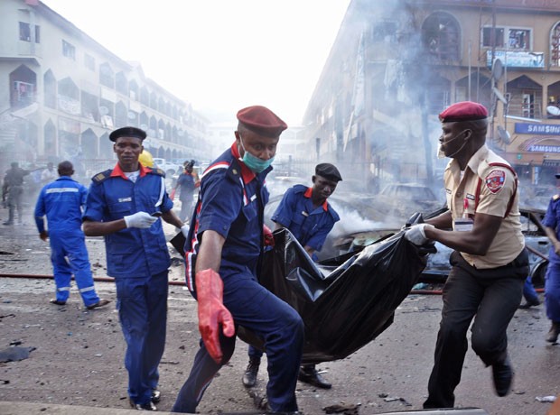 Policiais carregam corpo em saco plástico após explosão que deixou mortos em Abuja, na Nigéria, nesta quarta-feira (25) (Foto: Gbemiga Olamikan/AP)