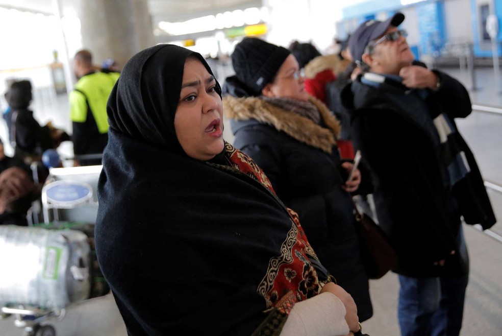 Mulher aguarda família chegar no aeroporto internacional John F. Kennedy, em Nova York, neste sábado (28)  (Foto: Andrew Kelly/Reuters)