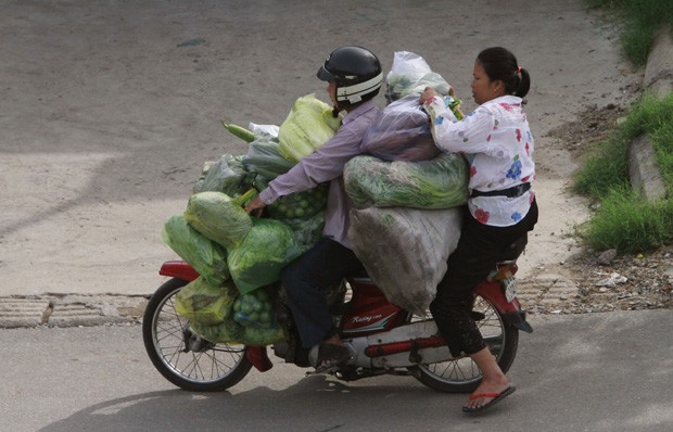 Casal precisou fazer esforço para se 'espremer' em moto supercarregada de legumes em Phnom Penh (Foto: Heng Sinith/AP)