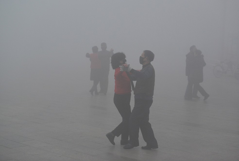 Pessoas usando máscaras dançam em praça em dia poluído em Fuyang, na China, nesta terça-feira (3) (Foto: China Daily/Reuters)