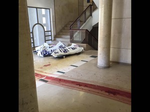 Marcas de sangue de corpos arrastados são vistas no chão da sinagoga palco do ataque a machados e facas em um bairro ultra-ortodoxo de Jerusalém. Ao fundo, corpos cobertos (Foto: Reuters/Zaka)