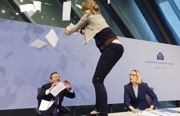 ADDS NAME OF THE WOMAN AT RIGHT - An activist stands on the table of the podium throwing paper at ECB President Mario Draghi, left, as Christine Graeff, Director General of Communications, looks on during a press conference of the European Central Bank, E (Foto: AP)