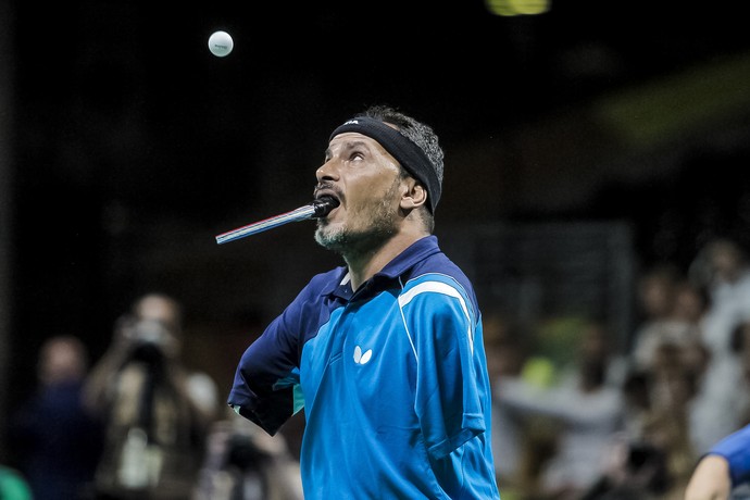 Descrição da imagem: Ibrahim Hamadtou prestes a sacar a bolinha de tênis de mesa com a raquete na boca (Foto: ITTF) Descrição da imagem: Ibrahim Hamadtou prestes a sacar a bolinha de tênis de mesa com a raquete na boca (Foto: ITTF)