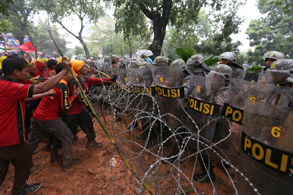 Participantes de marcha do Dia do Trabalhador tentam tirar do caminho cerca de arame farpado e entram em confronto com a polícia enquanto tentam ir em direção ao palácio presidencial em Jacarta, na Indonésia; milhares de trabalhadores pedem aumento do salário mínimo, fim da tercerização, assistência médica gratuita e melhores condições de trabalho (Foto: Dita Alangkara/AP)