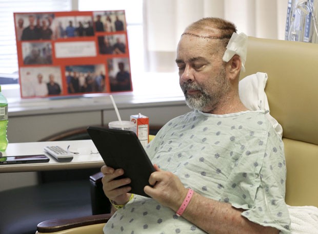 O paciente de transplante sorri lê em seu tablet na quarta-feira (3), ainda em recuperação da cirurgia (Foto: Pat Sullivan/AP)