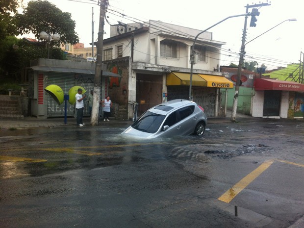 Imagem registrada por leitar mostra carro em cratera quando o nível da água ainda estava alto, alagando parte da rua. (Foto: Henrique Cruz Gomes/VC no G1 )