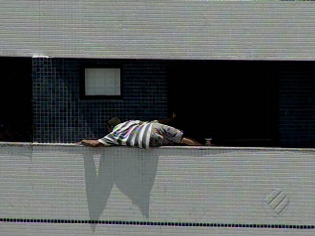 Operário chega a se deitar sobre parapeito de prédio durante trabalho de manutenção. (Foto: Reprodução / TV Liberal)