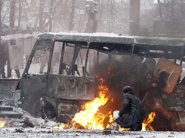 Homem se esconde atrás de ônibus incendiado enquanto as forças policiais avançam contra os manifestantes nesta quarta-feira (22). (Foto: Vasily Fedosenko/Reuters)