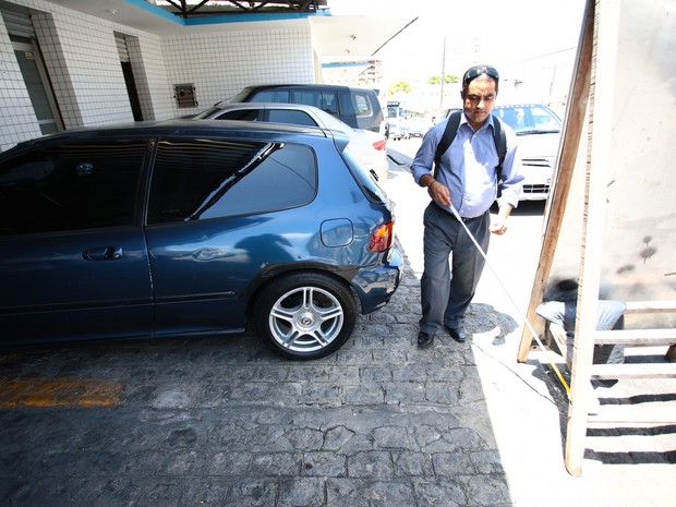 José Cícero te dificuldade passa passar entre placa e veículo estacionado na calçada. (Foto: Jonathan Lins/G1)