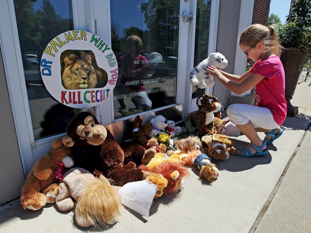 Autumn Fuller, de dez anos, coloca um bicho de pelúcia na entrada da clínica River Bluff Dental, do dentista Walter James Palmer, acusado de matar o leão Cecil, no Zimbábue (Foto: Reuters/Eric Miller)