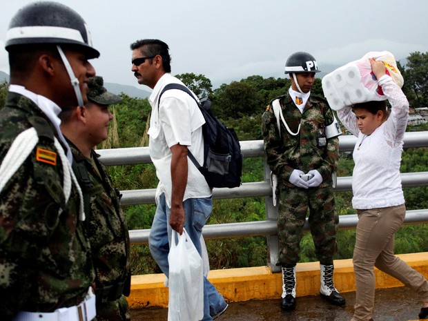 Uma jovem carrega papel higiénico quando ela cruza a fronteira colombiana -venezuelana sobre a ponte internacional Simón Bolívar depois de fazer compras , enquanto um policial colombiano olha. (Foto: REUTERS/Carlos Eduardo Ramirez)