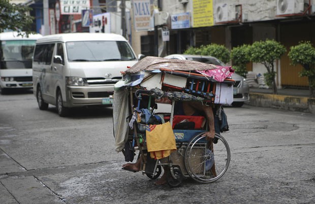 Homem anda em cadeira de rodas supercarregada nas Filipinas nesta quarta-feira (17) (Foto: Aaron Favila/AP)