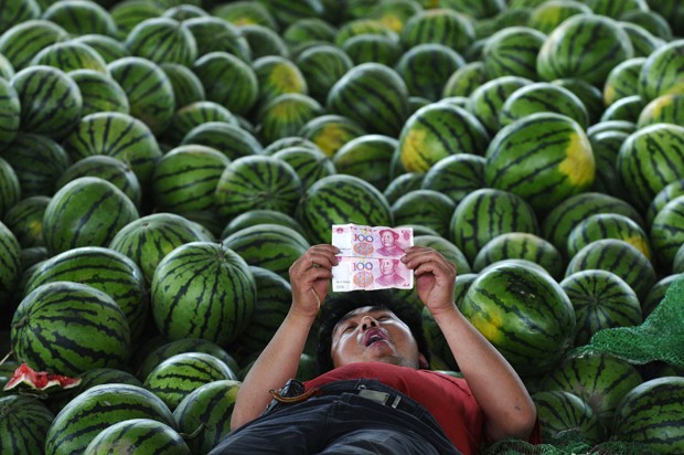 Em pose 'preguiosa', vendedor foi visto deitado entre melancias 'contemplando' notas de dinheiro em mercado de Changzhi, na China (Foto: Stinger/Reuters)