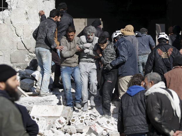 Pessoas ajudam um homem ferido após ataque russo contra prisão da Al-Qaeda na Síria neste sábado (9) (Foto: REUTERS/Khalil Ashawi)