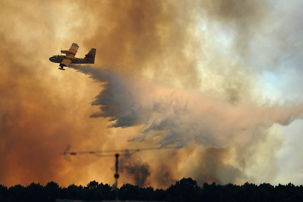 Um avião de combate a incêndios despeja água sobre um incêndio perto da aldeia de Pedrogão Grande, em Portugal. Mais de 2 mil bombeiros lutam para conter grandes incêndios florestais na região central do país (Foto: Paulo Duarte/AP)
