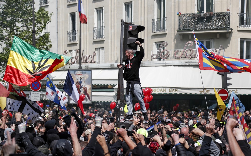 Manifestantes se reúnem no distrito de Montparnasse, em Paris, durante protestos pelo Dia do Trabalho, nesta quarta-feira (1º), enquanto um homem sobe em um semáforo e gesticula. — Foto: Zakaria Abdelkafi / AFP