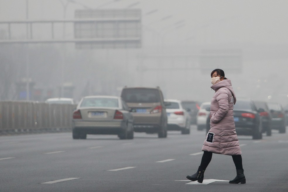 Mulher atravessa via movimentada em Pequim, na China, usando máscara para se proteger da poluição (Foto: AP Photo/Andy Wong)