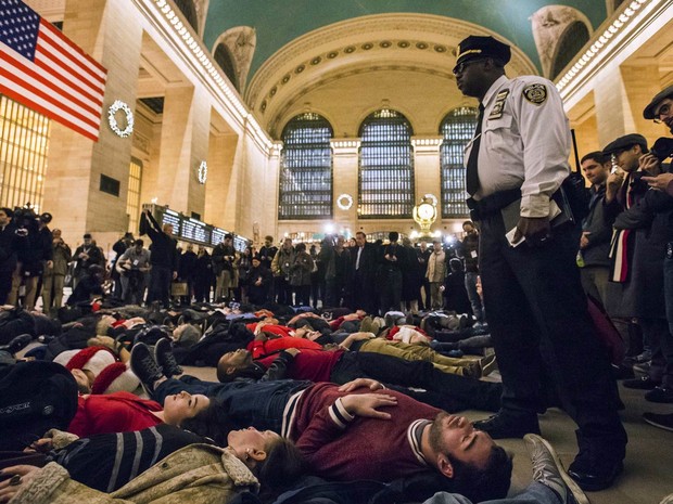 Policial observa ativistas no chão do terminal Grand Central, no centro de Nova York, nos EUA. O protesto na hora do rush pede justiça no caso de Eric Garner. Um júri decidiu livrar de acusações o policial branco que matou o homem negro por enforcamento (Foto: Adrees Latif/Reuters)