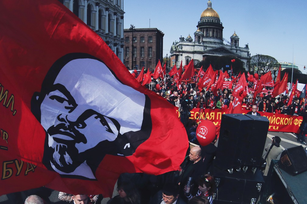 Apoiadores do partido comunista russo carregam uma bandeira com o rosto do fundador da União Soviética, Vladimir Lênin, durante um protesto de 1º de maio em São Petersburgo, na Rússia. — Foto: Dmitri Lovetsky/AP