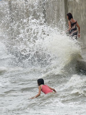 Crianças brincam em ondas causadas pelo tufão Utor nas Filipinas nesta segunda-feira (12) (Foto: Jay Directo/AFP)