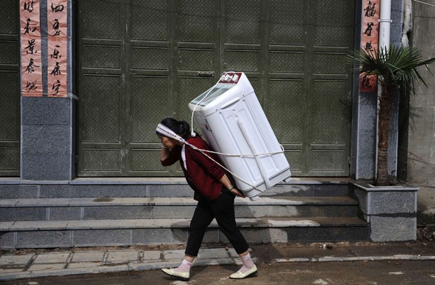 30 de julho - mulher foi fotografada carregando uma máquina de lavar roupa nas costas em Dali, na província de Yunnan, na China (Foto: Stringer/Reuters)