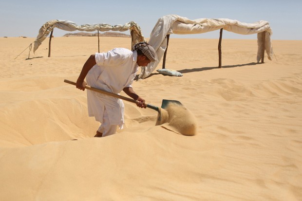 Funcionário cava buraco para enterrar paciente na areia do oásis de Siwa (Foto: Reuters/Asmaa Waguih) Funcionário cava buraco para enterrar paciente na areia do oásis de Siwa (Foto: Reuters/Asmaa Waguih)