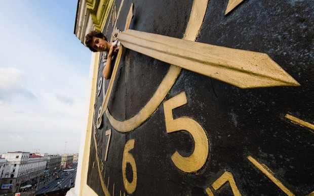 O explorador Kirill Vselensky dai de dentro de relógio, no topo do principal edifício da KGB em Minsk, Belarus. (Foto: Raskalov-Vit.Livejournal.com/BBC)