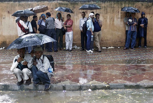 Indianos se protegem da chuva em Nova Déli nesta segunda-feira (5) (Foto: Anindito Mukherjee/Reuters)