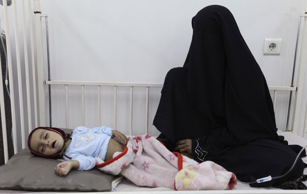 Mulher aguarda pelo atendimento a sua  que, cansada, dorme ao seu lado (Foto: Mohamed al-Sayaghi/Reuters)