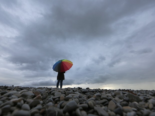 Mulher protege-se da chuva em uma praia de Nice, no sul da França, neste sábado (15). (Foto: Reuters//Eric Gaillard )