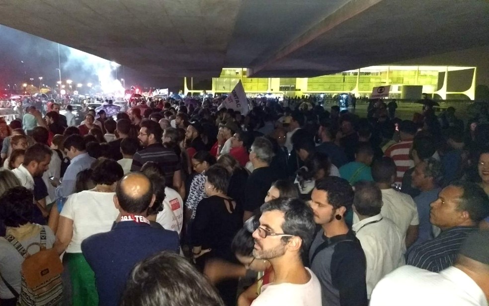 Manifestantes se escondem da chuva em ato na Praça dos Três Poderes, em Brasília; ao fundo, grupo estoura rojões (Foto: Marília Marques/G1)