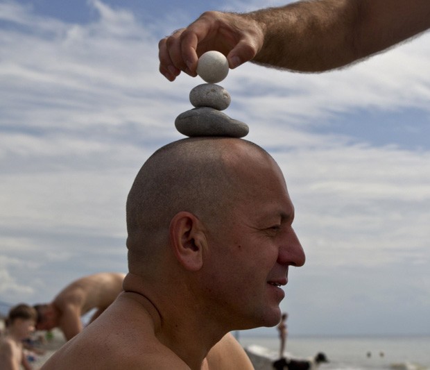 No topo da cabeça de Alexander, o engenheiro Yuri ergue uma pirâmide de pedras em praia de Sochi, na Rússia (Foto: Maxim Shemetov/Reuters)