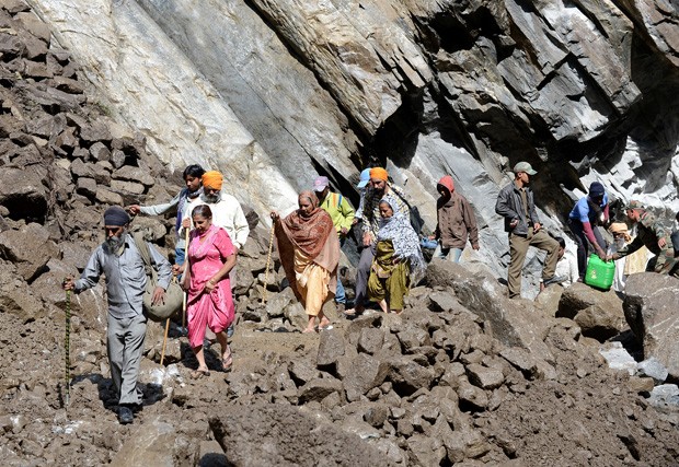 Peregrinos e moradores de vilarejos próximos fazem travessia em meio a pedras que deslizaram da montanha de Govindghat, como consequência das fortes chuvas na região (Foto: Sajjad Hussain/AFP)