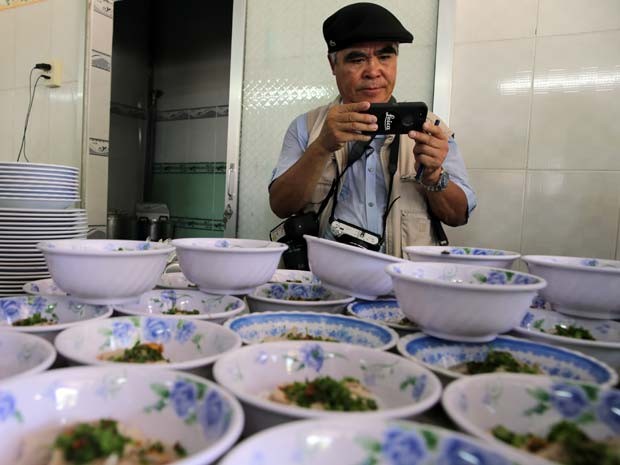 Nick Ut usa um smartphone para tirara uma foto em restaurante da família de Kim Phuc, menina que registrou há mais de 40 anos na Guerra do Vietnã (Foto: AP Photo/Na Son Nguyen)