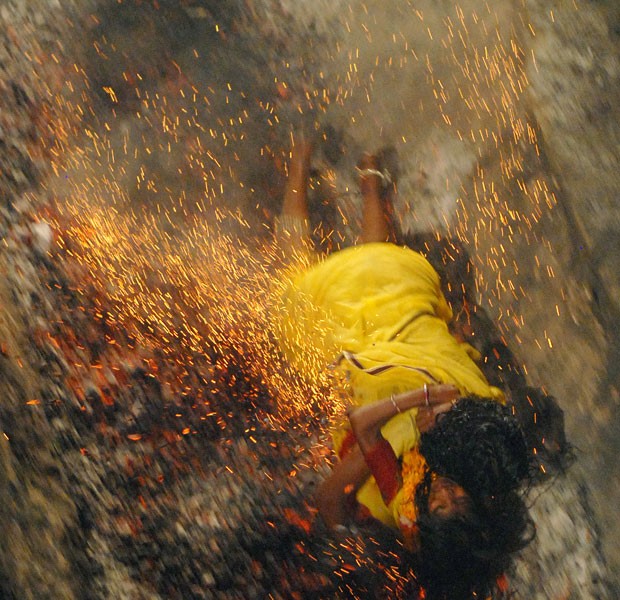 Devota hindu cai em carvão quente enquanto segura a filha durante uma corrida sobre carvão na Índia (Foto: Shammi Mehra/AFP)