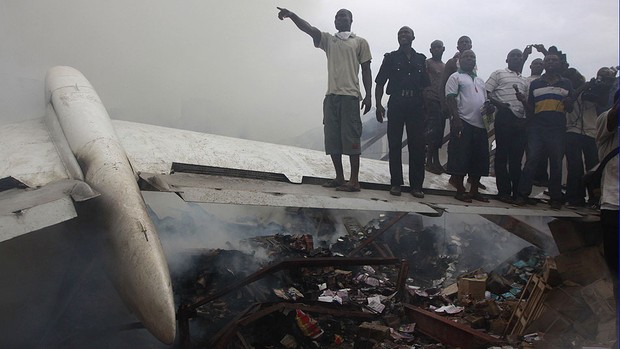 Moradores do local do acidente sobem numa das asas do avião que caiu em Lagos, na Nigéria (Foto: Sunday Alamba/AP)