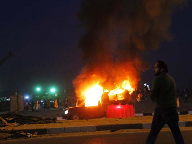 Torcedor é visto perto de carro policial que pega fogo após confrontos entre policiais e torcedores perto de estádio de futebol no Cairo (Foto: REUTERS/Stringer)